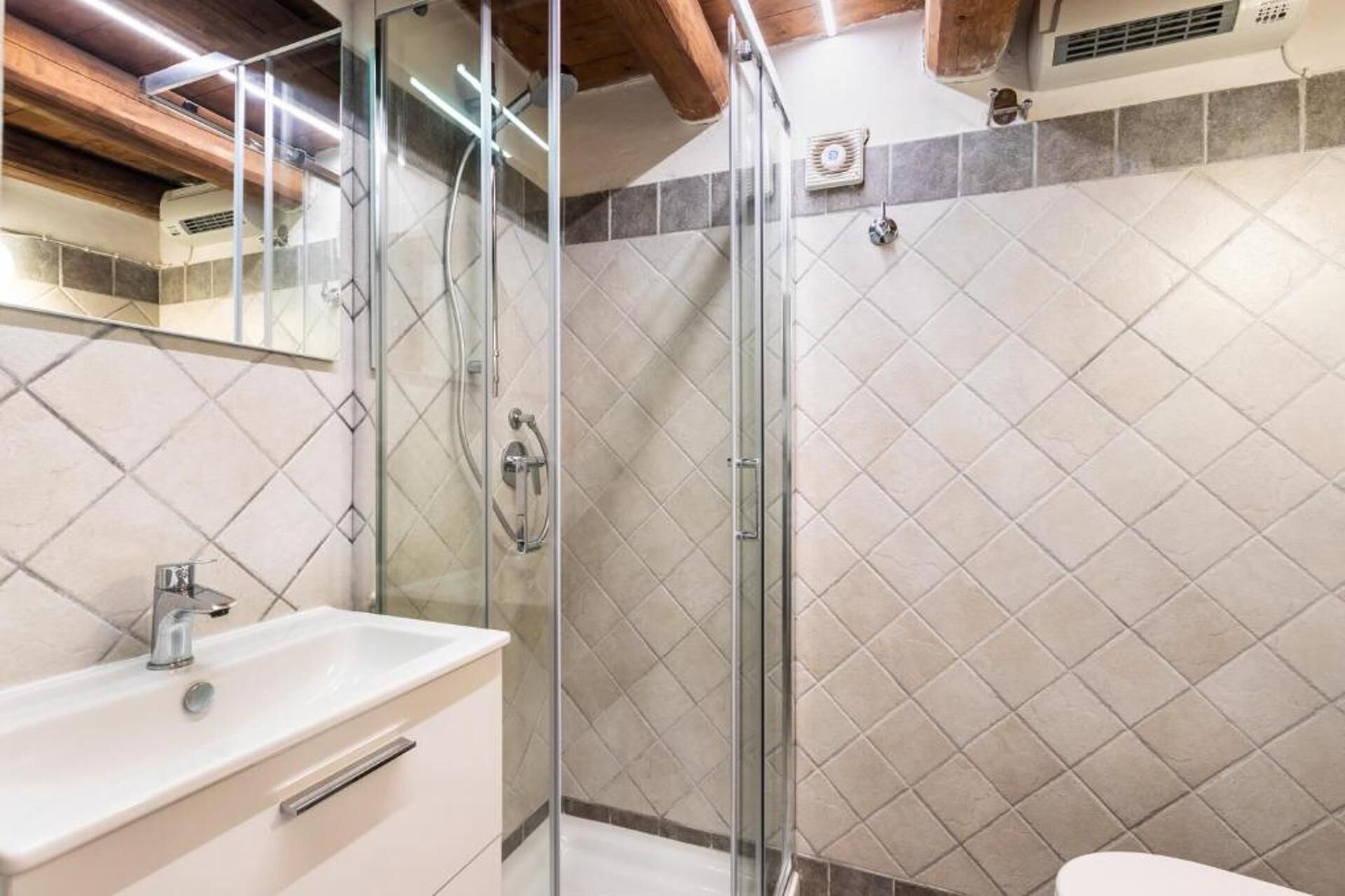 Une salle de bain moderne avec une douche à parois de verre, un lavabo blanc et un mur recouvert de carreaux.