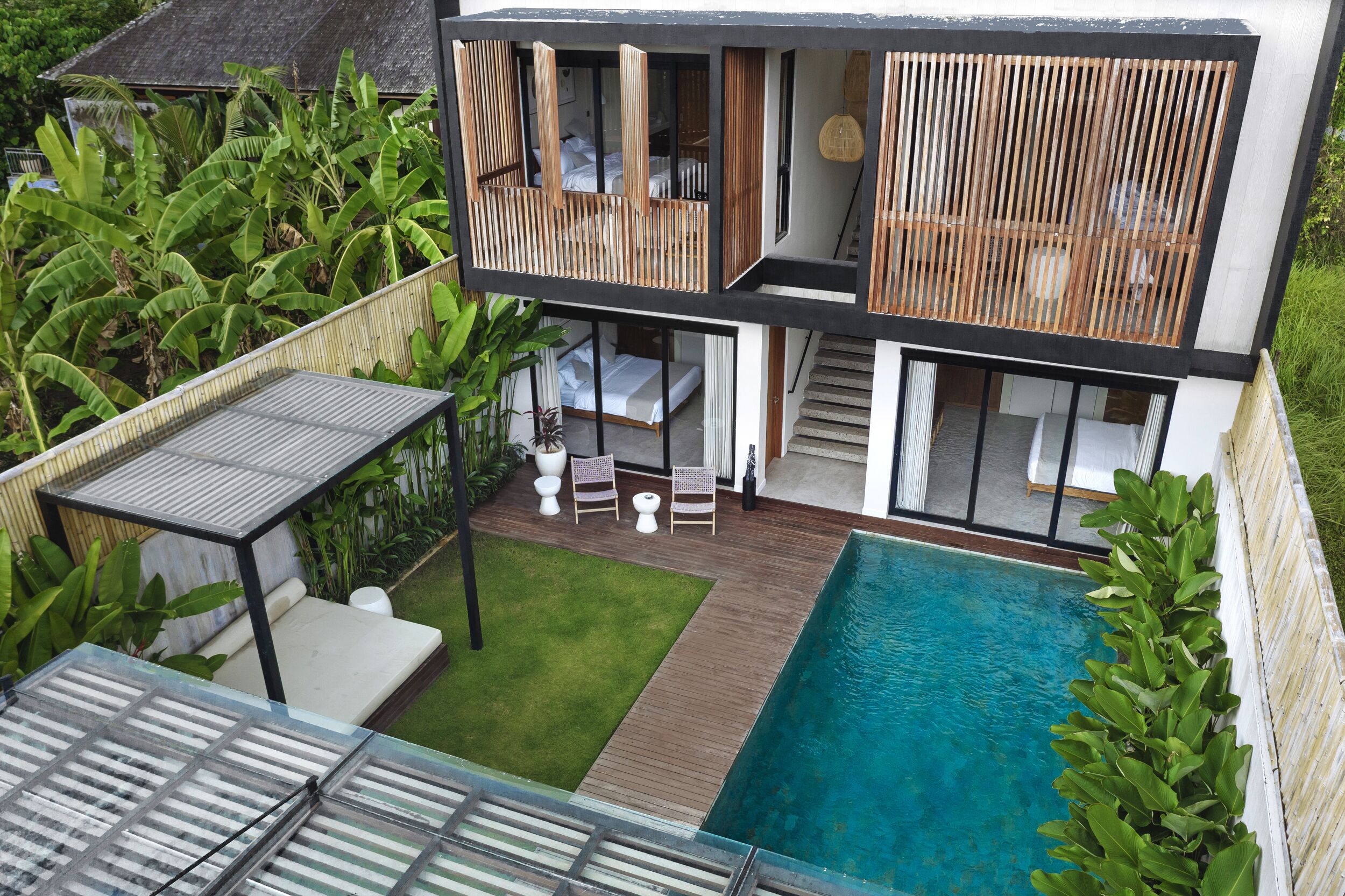 Una casa moderna de dos pisos con piscina, mobiliario exterior y abundante vegetación.
