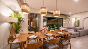 A modern dining area with a wooden table set for six, surrounded by wooden chairs with grey cushions. There are three hanging pendant lights above the table. - RED SUNSET VILLA CANGGU 5 MIN WALK BEACH (Canggu)