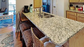 A kitchen with a granite countertop, a sink, wooden cabinets, and a refrigerator. - Inlet Point 15B, Beautifully Furnished Condo, Near Beach & Creek (Pawleys Island)