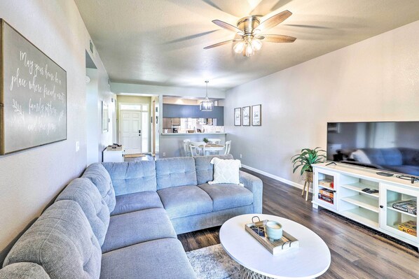 A modern living room with a sectional sofa, a white coffee table, and a TV on a white cabinet. - Golf Course Views & Pool Access: Glendale Condo! (Glendale)