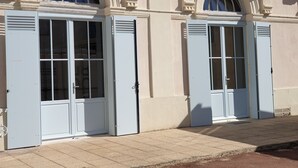 En byggnadsfasad med två stora, vita, dubbeldörrar med glaspartier, utformad i en klassisk arkitektonisk stil med utsmyckade detaljer ovanför dörrarna.
