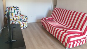Ett rum med en randig röd och vit soffa, en färgglad fåtölj och en platt-TV som står på ett stativ.