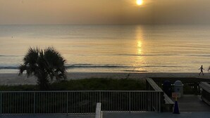 Ein Sonnenuntergangsblick vom Balkon mit Blick auf das Meer, mit einer Palme und einem hölzernen Weg, der zum Strand führt.