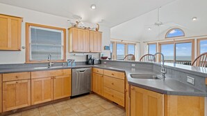 A spacious kitchen with wooden cabinets, a dishwasher, and a large window overlooking the ocean. - Windscape Soundfront in Frisco Incredible Views 400ft to Beach Access! (Frisco)