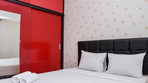 Une chambre d’hôtel avec une armoire rouge, un papier peint à motifs floraux, une tête de lit noire recouverte de tissu et du linge de lit blanc.