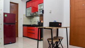 Une cuisine compacte avec des meubles de rangement rouges, un réfrigérateur, un four à micro-ondes et une petite table avec des tabourets.