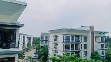A modern multi-story residential building with balconies, a parking area, and surrounding greenery.