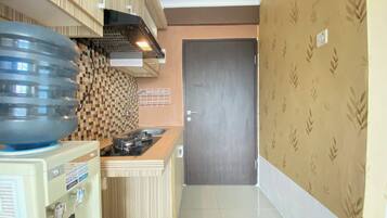A compact kitchen with a water dispenser, a stove, and a patterned backsplash.