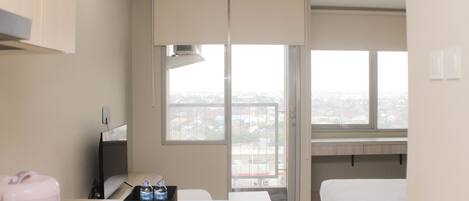 A hotel room with a bed, a desk with a computer, a window with a city view, and a minibar.