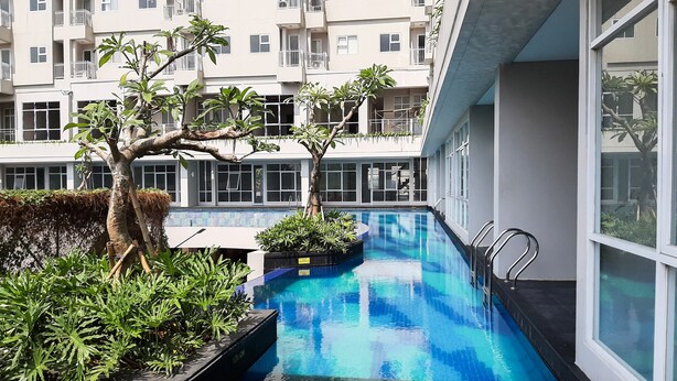 A swimming pool with a 120 cm depth, surrounded by greenery and modern buildings. - Comfort And Best Choice 2Br At Bintaro Icon Apartment (South Tangerang)