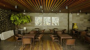 Un restaurante de diseño moderno, con listones de madera en el techo, una gran planta en maceta y vistas a través de tres ventanales.