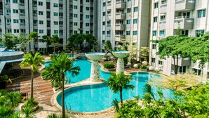 Un hotel moderno con varios pisos, una piscina central rodeada de palmeras y una terraza en la azotea.