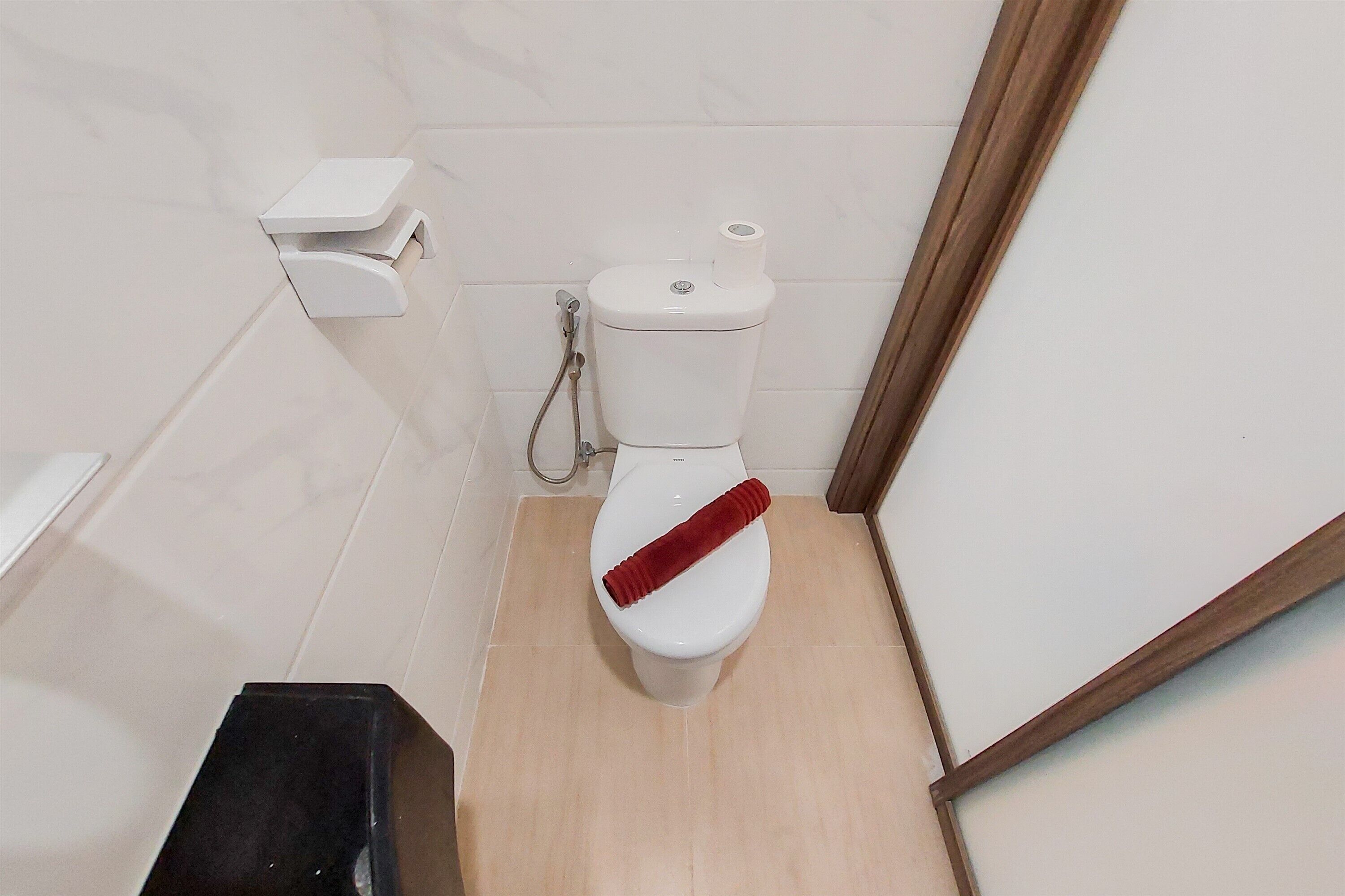 Un baño pequeño con un inodoro blanco, un dispensador de papel higiénico blanco y suelo de madera.