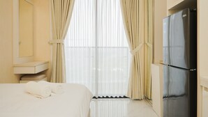 A hotel room with a bed, a built-in wardrobe, a minibar, and a large window with curtains.