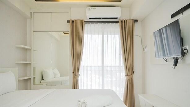 Ein modernes Hotelzimmer mit Bett, integriertem Kleiderschrank, Nachttisch und Wand-Fernseher.