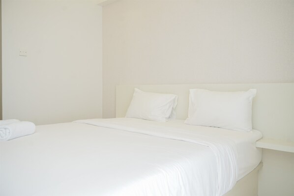 Una cama bien hecha con ropa blanca y almohadas en una habitación con paredes lisas y un cabecero sencillo.