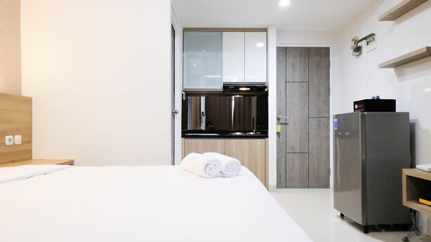Ein kleines Hotelzimmer mit Bett, einer kompakten Küchenzeile und einem Kühlschrank.