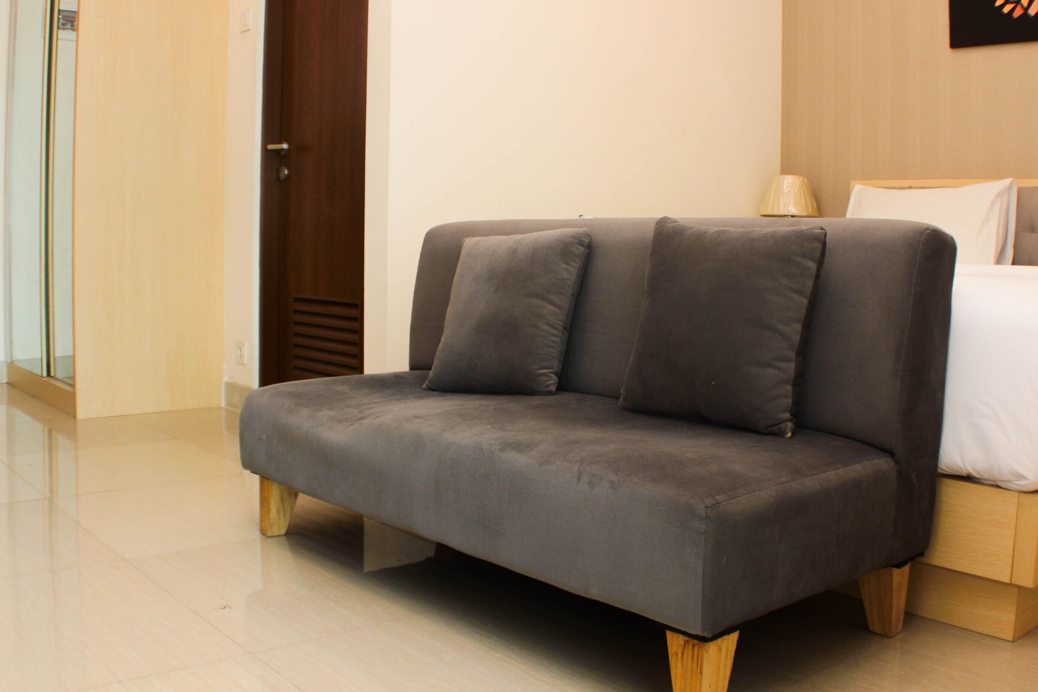 Quarto moderno com sofá cinza, estrutura de cama de madeira e porta de madeira.