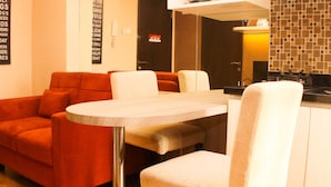 A modern kitchen with a wooden table and chairs, a red sofa, and a tiled backsplash. - Strategic And Simply 2Br At Bassura City Apartment (Jakarta)