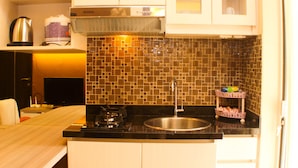 A kitchen with a black countertop, stainless steel sink, and a tiled backsplash. - Strategic And Simply 2Br At Bassura City Apartment (Jakarta)