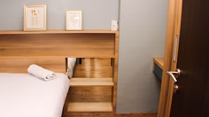 A bedroom with a wooden bed, a small wooden shelf with framed pictures, and a door. - Strategic And Simply 2Br At Bassura City Apartment (Jakarta)