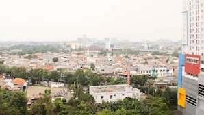A cityscape with a mix of residential and commercial buildings, including a prominent high-rise with a distinctive red and blue facade. - Great Location And Simply Studio Room At Bassura City Apartment (Jakarta)
