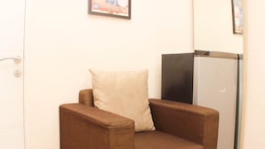 A small, brown armchair with a cushion, positioned next to a white refrigerator in a room with white walls. - Great Location And Simply Studio Room At Bassura City Apartment (Jakarta)