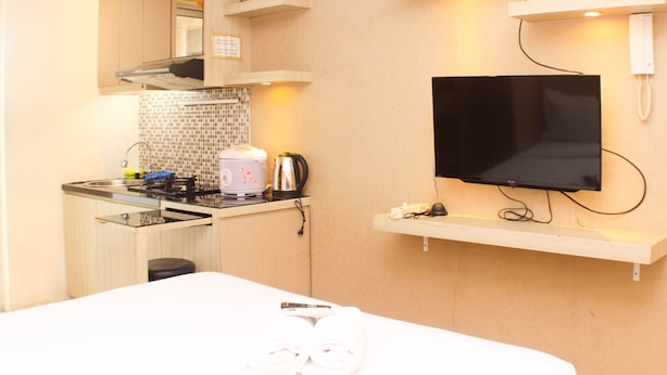 A compact kitchen with a microwave, kettle, and a flat-screen TV mounted on the wall. - Great Location And Simply Studio Room At Bassura City Apartment (Jakarta)