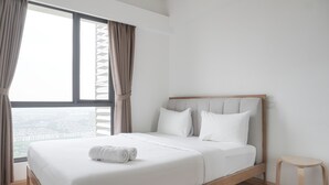 A modern bedroom with a large bed, white bedding, and a view of a cityscape through the window. - Homey And High Floor 2Br At Sky House Bsd Apartment (Pagedangan)