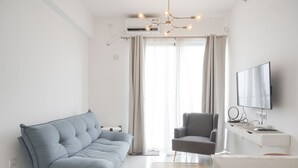A modern living room with a sofa, armchair, and a TV on a stand. - Homey And High Floor 2Br At Sky House Bsd Apartment (Pagedangan)