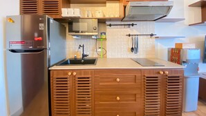 A modern kitchen with a built-in refrigerator, microwave, and stove. There are wooden cabinets with ventilation slats and a stainless steel sink. - Spacious 2Br Apartment Tamansari Tera Residence (Bandung)