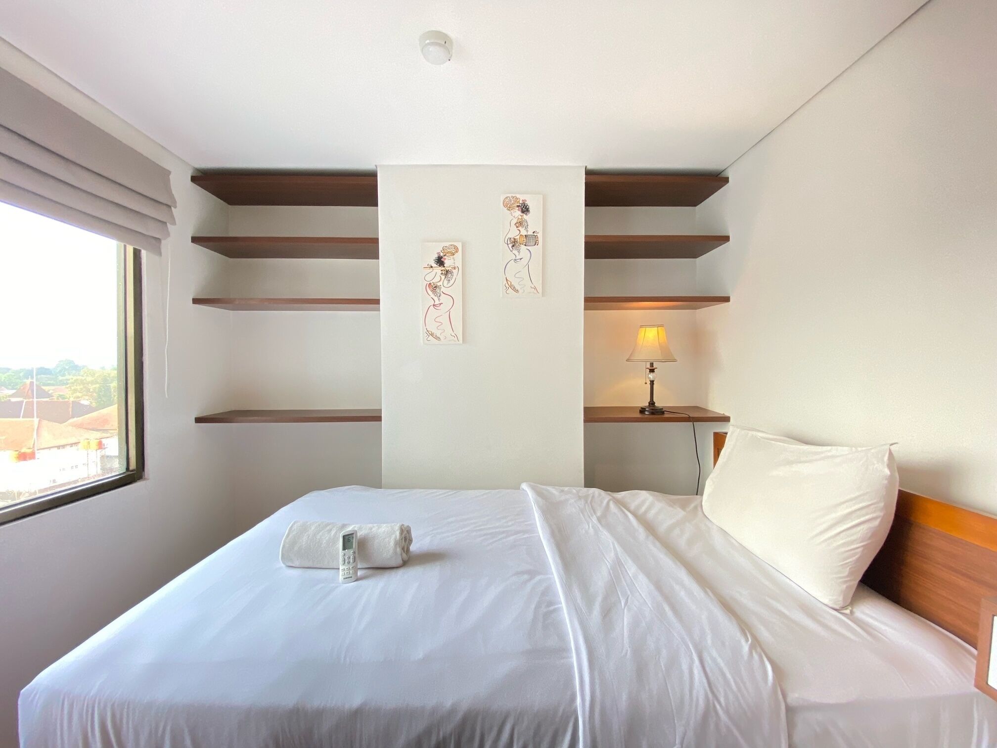 A hotel room with a neatly made bed, a bedside lamp, and artwork on the wall.