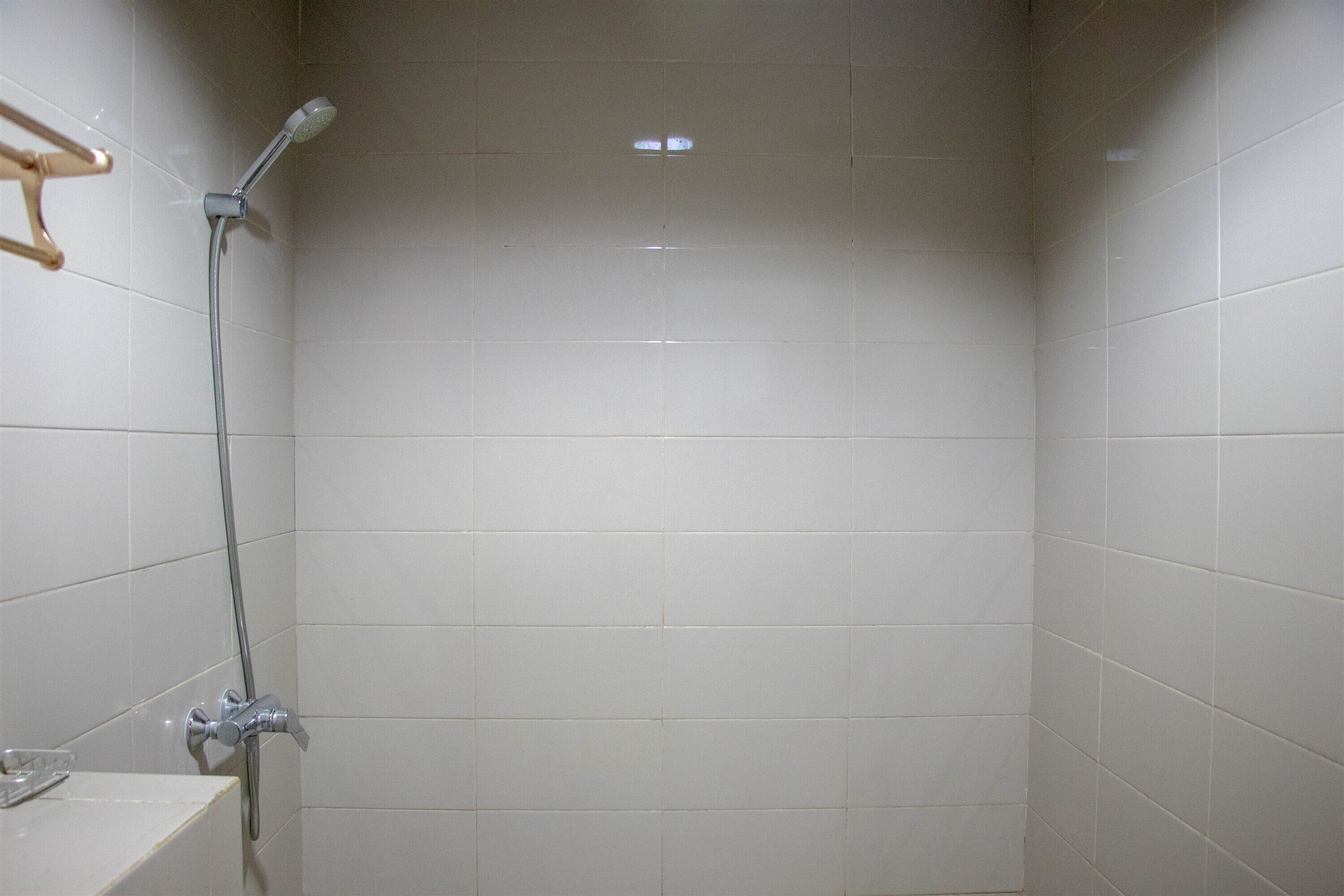 A bathroom with white tiled walls, a shower with a handheld showerhead, and a towel rack.