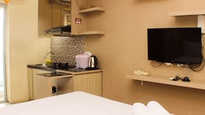 Ett hotellrum med en säng, ett litet pentry, en tv som är monterad på väggen och en hylla med ett par tofflor.