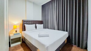 Una habitación de hotel con una cama grande, una mesita de noche con lámpara y cortinas oscuras.