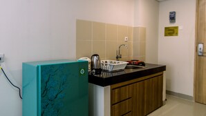A compact kitchen with a teal refrigerator, a black countertop, and wooden cabinets. - Comfort Studio Apartment At Padina Soho Residence (Tangerang)