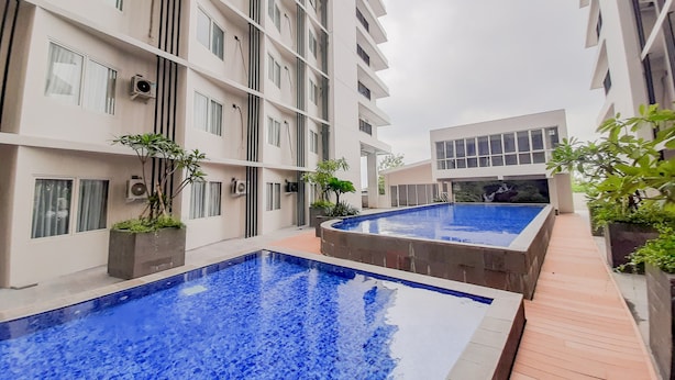 A modern building with two swimming pools, surrounded by balconies and potted plants. - Comfort Studio Apartment At Padina Soho Residence (Tangerang)
