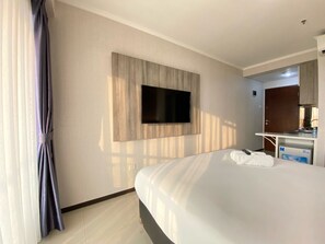 Ein Hotelzimmer mit Bett, Flachbildfernseher an der Wand, einer kleinen Küchenzeile und einem Fenster mit Vorhängen.