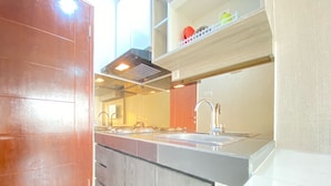 A modern kitchen with a double sink, wooden cabinets, and a stainless steel range hood. - Comfy Studio At Gateway Pasteur Apartment (Cimahi)