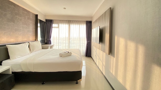 A modern hotel room with a large bed, a flat-screen TV mounted on the wall, and a desk with a chair. - Comfy Studio At Gateway Pasteur Apartment (Cimahi)