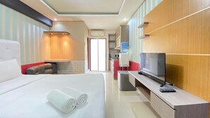A hotel room with a large bed, a TV, a desk, and a seating area with a sofa and armchair. - Spacious Studio Furnished Apartment At Gateway Ahmad Yani Cicadas Bandung (Bandung)