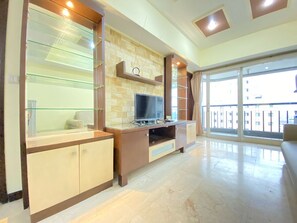 A modern living room with a flat-screen TV, glass shelving, and a large sliding glass door leading to a balcony. - Spacious And Modern 2Br At Braga City Walk Apartment (Bandung)