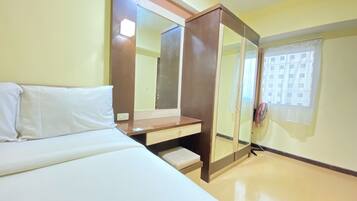 Habitación de hotel con cama, mesita de noche de madera, espejo y ventana con vista a edificios.