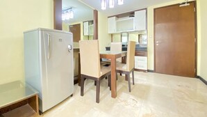 A compact kitchen with a refrigerator, a dining table with chairs, and a wooden door. - Spacious And Modern 2Br At Braga City Walk Apartment (Bandung)