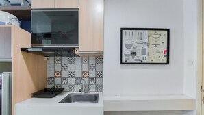 A compact kitchen with a microwave, sink, and patterned backsplash. - Nice And Elegant Studio At Tree Park City Bsd Apartment (South Tangerang)