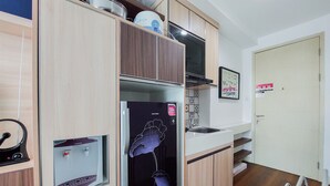 A compact kitchen with wooden cabinets, a built-in microwave, and a water dispenser. - Nice And Elegant Studio At Tree Park City Bsd Apartment (South Tangerang)