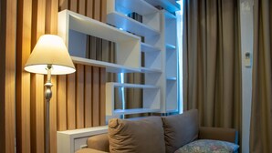 A modern living room with a sofa, a lamp, and built-in shelves. - Nice And Cozy 1Br With Extra Room Apartment At Capitol Park Residence (Jakarta)