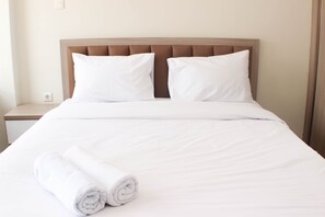 A neatly made bed with white linens and pillows, a rolled white towel on the side, and a wooden headboard. - Nice And Elegant Studio Apartment At Mustika Golf Residence (Cikarang)