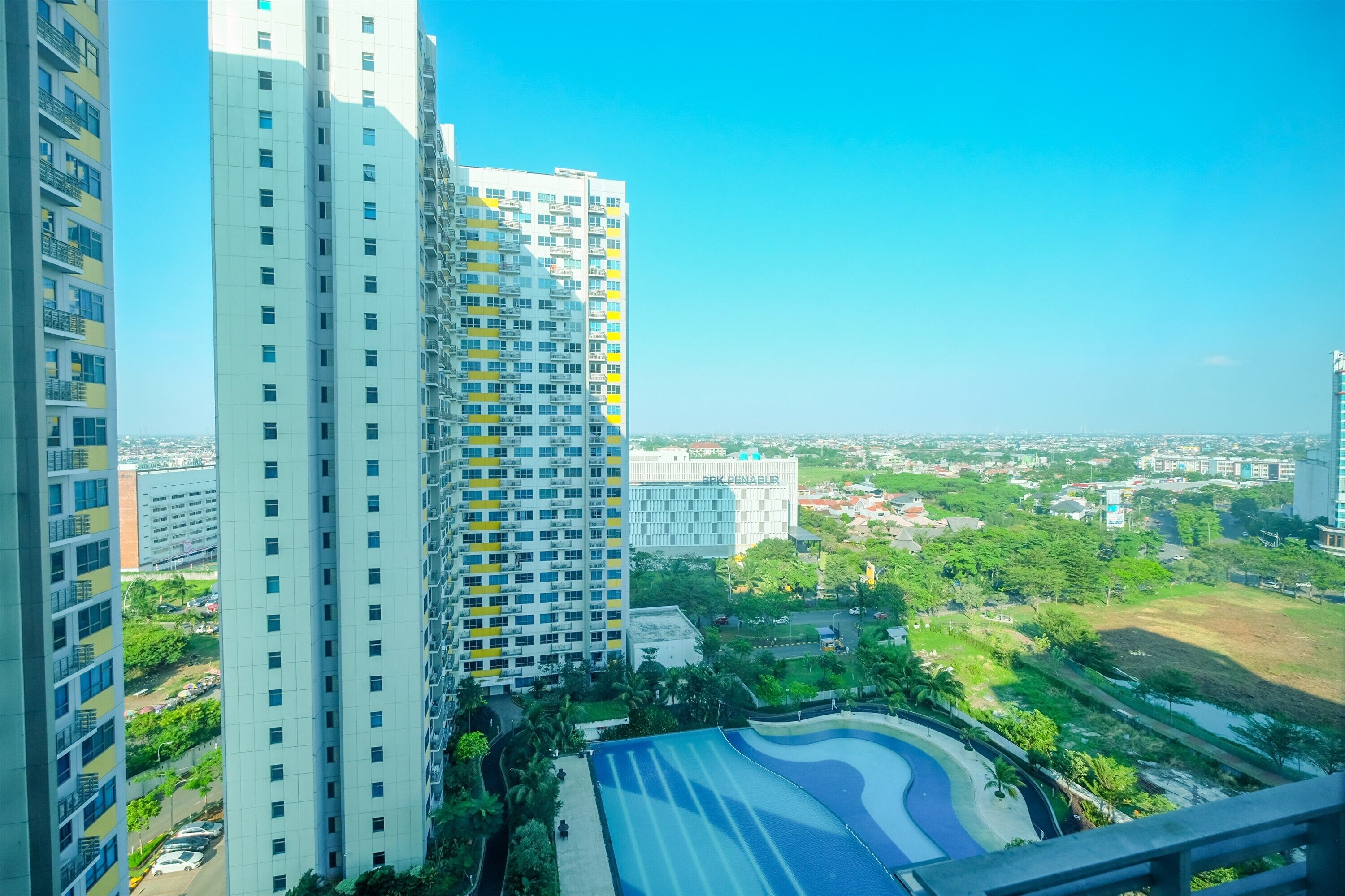 A high-rise building with multiple floors, a swimming pool, and surrounding greenery.